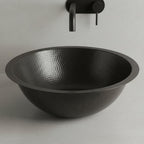 Black hammered sink with a black faucet on a light gray background