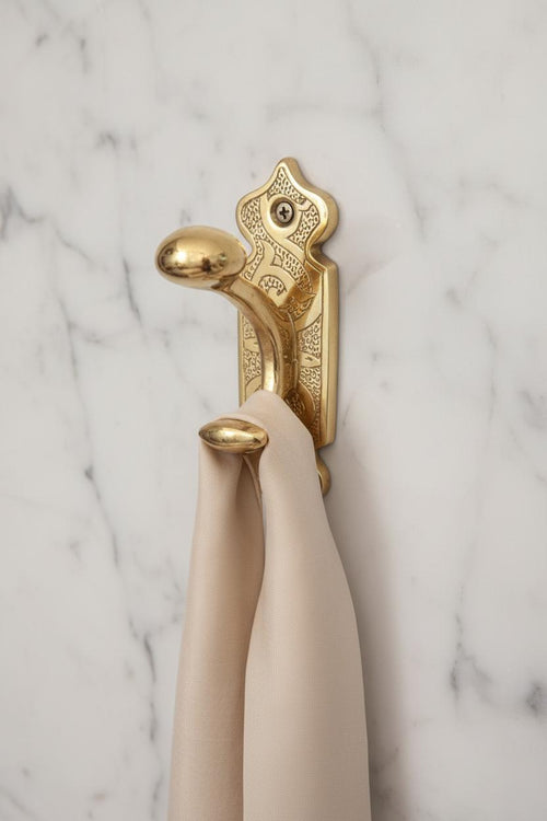 Decorative gold towel hook with beige towels on a marble wall.