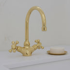 Gold faucet on a white sink with a bar of soap in the background