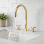 Gold kitchen faucet and handles on a white tiled wall with a sink.