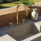 Gold faucet over a concrete sink with a wooden bench and plant in the background