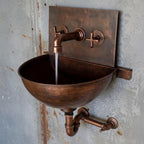 Vintage-style copper sink with faucet on a textured wall.