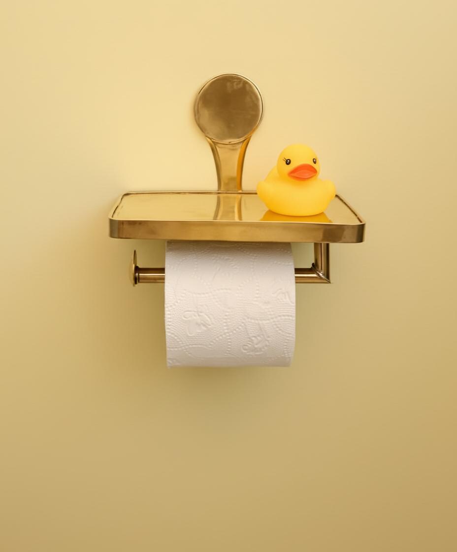 Gold toilet paper holder with a roll of toilet paper and a yellow rubber duck on a beige background