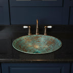 Decorative turquoise sink with bronze faucet on a black countertop against a dark blue cabinet.