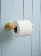 Gold toilet paper holder with a roll of toilet paper on a light blue wall.