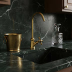 Gold faucet on a black marble countertop with a glass container and metal bucket.