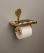 Gold wall-mounted holder with a smartphone and toilet paper roll on a beige background