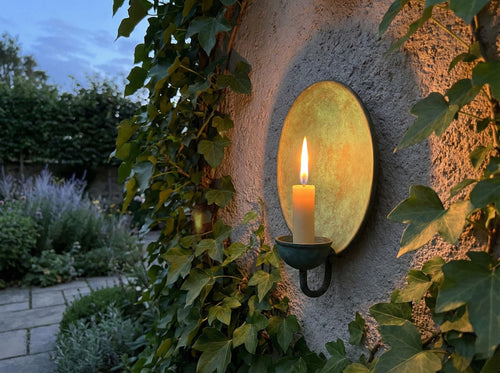 Candle in a wall-mounted metal holder on a stone wall with greenery