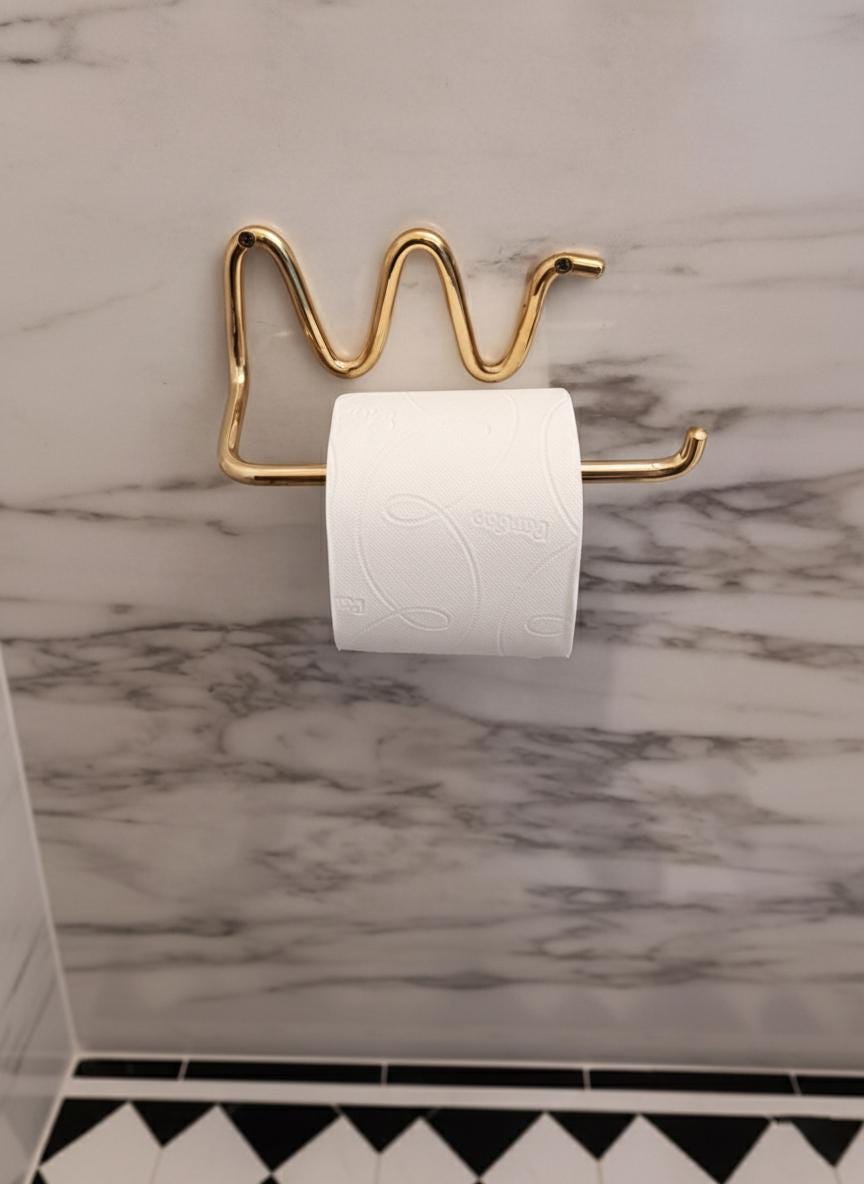 Gold toilet paper holder with a roll of toilet paper on a marble wall.