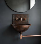 Bronze wall-mounted sink with copper fixtures against a dark gray wall.