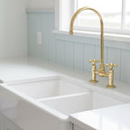 Gold kitchen faucet on a white sink with a light blue backsplash.