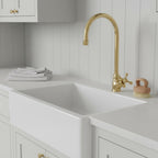 Kitchen sink with gold faucet and cleaning brush on white countertop