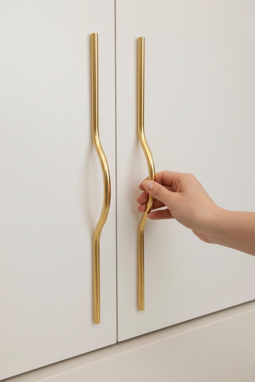 Hand opening a white cabinet door with gold handles.
