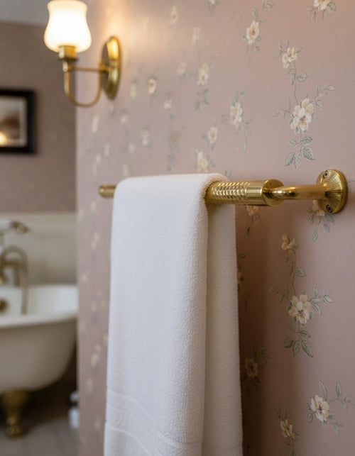 White towel hanging on a gold towel rack against a floral wallpapered wall.