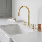 Kitchen sink with gold faucet and accessories on a white countertop.