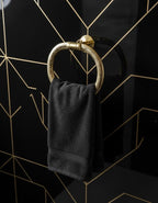 Black towel hanging on a gold towel ring against a black tiled wall with geometric patterns.
