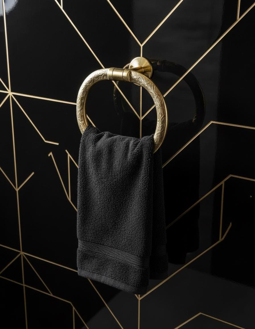 Black towel hanging on a gold towel ring against a black tiled wall with geometric patterns.