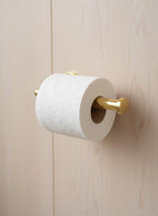 Gold toilet paper holder with a roll of toilet paper on a wooden wall.