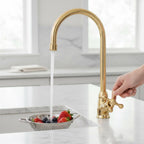 Gold kitchen faucet with water flowing into a sink containing fruits and vegetables.