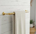 Gold towel bar with a beige towel on a white wooden wall