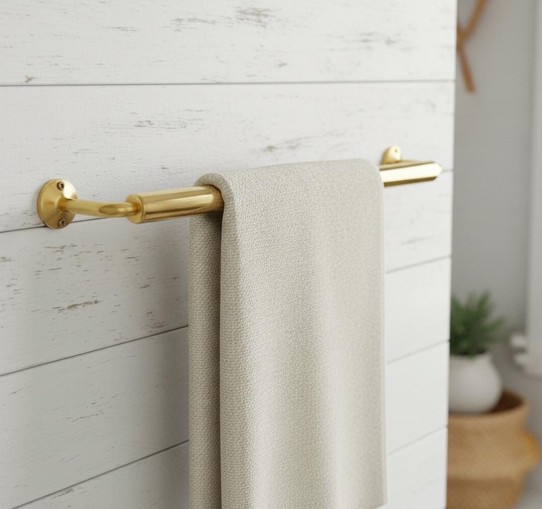 Gold towel bar with a beige towel on a white wooden wall
