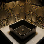 Black sink with gold faucet against a decorative gold and black wall.