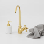 Gold kitchen faucet with a white soap dispenser and gray towel on a light gray background