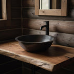 Black hammered sink on a wooden countertop with a wooden wall and mirror in the background