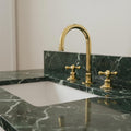 Gold faucet on a green marble countertop with a white sink.