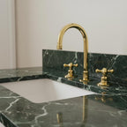 Gold faucet on a green marble countertop with a white sink.