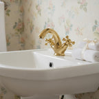 White sink with gold faucet and floral wallpaper