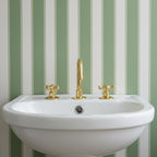 White sink with gold faucet and handles against a green and white striped wall.