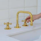 Gold faucet set on a white sink with a tiled wall background