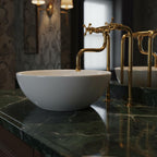 White ceramic sink with gold faucet on a green marble countertop in a bathroom setting.