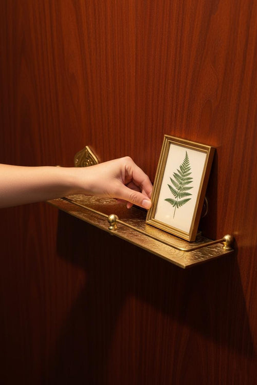 Hand placing a framed fern print on a wooden shelf.