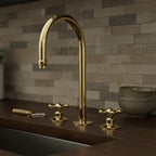 Gold kitchen faucet on a wooden countertop with a stone wall background