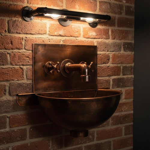 Vintage-style copper sink mounted on a brick wall with industrial lighting.