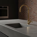 Gold faucet on a gray kitchen sink with a brick wall background