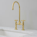 Gold kitchen faucet on a marble countertop with a light gray wall background