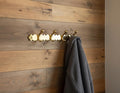 Gold hook with multiple hooks on a wooden wall with a gray towel hanging from one of them.