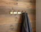 Gold hook with multiple hooks on a wooden wall with a gray towel hanging from one of them.