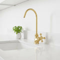 Gold kitchen faucet on a white countertop with a small plant in the background
