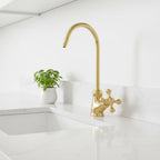 Gold kitchen faucet on a white countertop with a small plant in the background