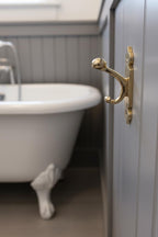 Gold hook on a bathroom cabinet with a white bathtub in the background