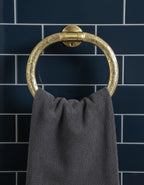 Brass towel ring with a gray towel against a dark blue tiled wall