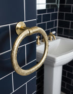Gold towel ring on a blue tiled wall with a white sink and gold faucet.