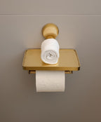 Gold toilet paper holder with a roll of toilet paper on a beige wall.