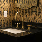 Bathroom sink with gold fixtures against a geometric patterned wall.