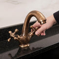 Bronze faucet being turned by a hand on a black countertop.