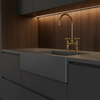 Modern kitchen sink with gold faucet against a wooden wall.
